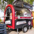 Foodtrailer bei Event mit schwarz-roter Folierung und offener Verkaufskalppe, Food Truck Werbung