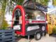 Foodtrailer bei Event mit schwarz-roter Folierung und offener Verkaufskalppe, Food Truck Werbung