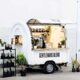 Vit kaffeförsäljningsvagn med öppen försäljningsklaff med många växter som dekoration 