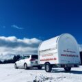 Auto fährt in Schneelandschaft mit mobilen Verkaufsanhänger